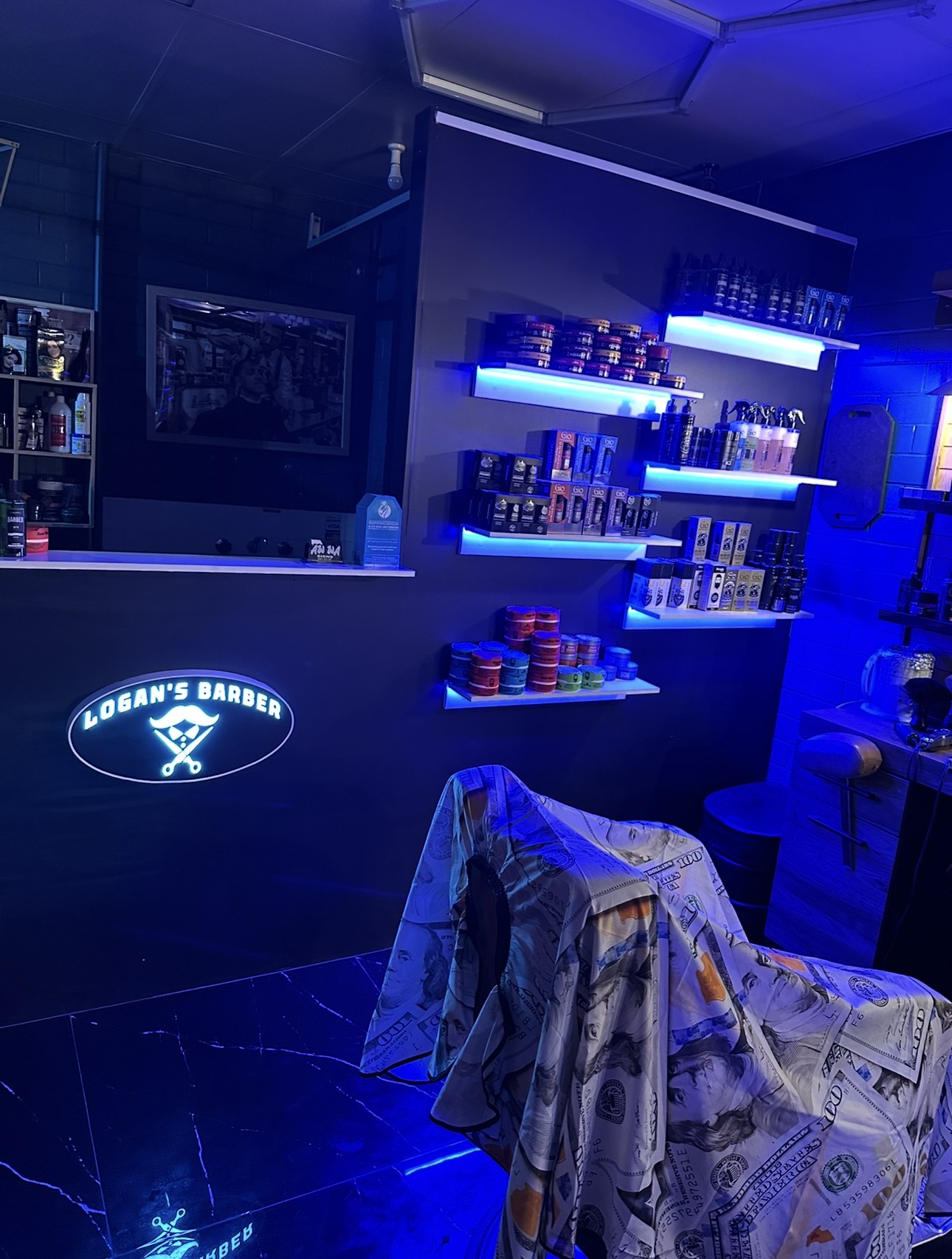The illuminated Logan's Barber sign and product shelves lit in blue