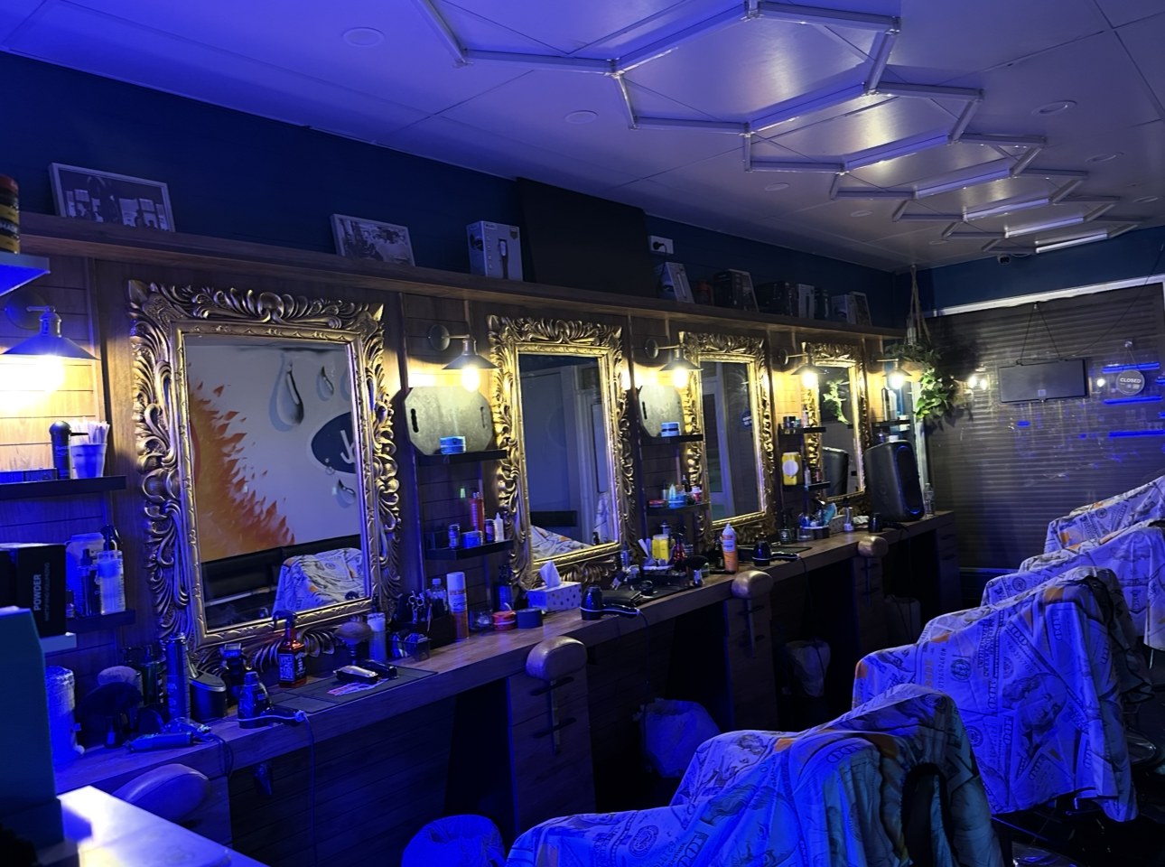 A row of gold baroque mirrors and timber workstations lit in blue