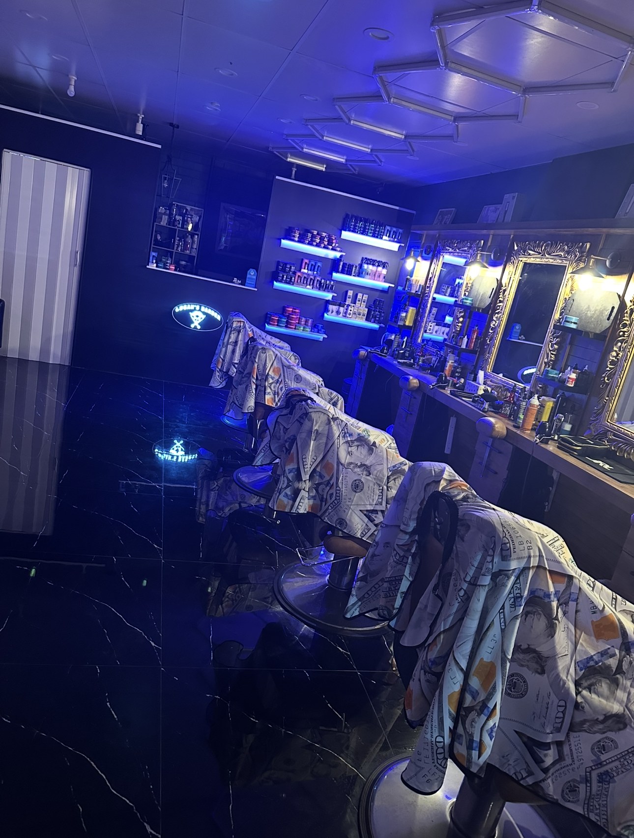Barber chairs in a row under blue lighting, with the lit shop sign on the back wall